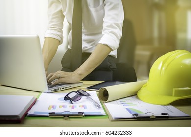 Engineer Hold Security Helmet And Blueprint Paper Construction Drawing Plan Near Laptop Computer,Architect Working In Office,Engineering Tools On Desk At Site Project