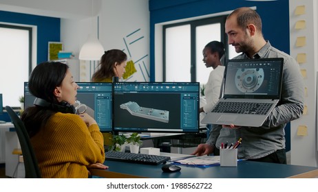 Engineer holding laptop and pointing on display showing to manager 3D gears image working in CAD program, compering with components from pc software. Team analysing technical prototype project