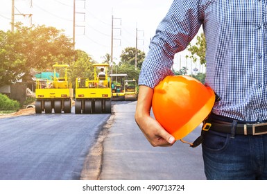 engineer holding safety helmet at road construction site with roller compactor working asphalt road. 
