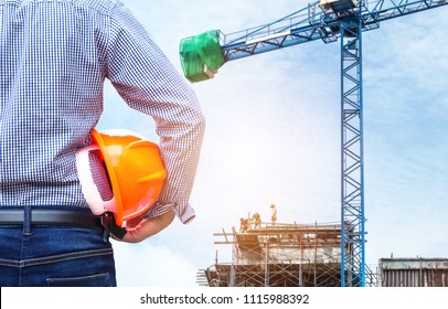 Engineer Holding Yellow Safety Helmet In Building Construction Site With Big Blue Crane