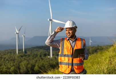 Engineer India man working with tablet at windmill farm Generating electricity clean energy. Wind turbine farm generator by alternative green energy. Asian engineer checking control electric power - Shutterstock ID 2228950383