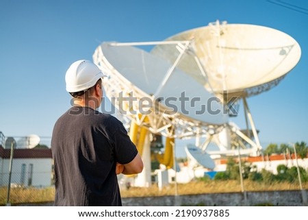 Engineer looking earth based astronomical radio telescope. Radio telescopes used in science for space observation and distant objects exploring. Caucasian man white protective helmet satellite dishes