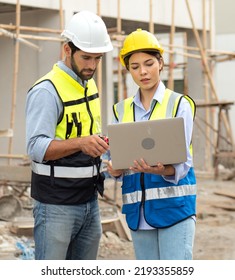 Engineer Man And Female Architect Wear Safety Helmets Discuss Housing Development Project At Construction Site Using Laptop Computer. Contractor Manager Inspecting House Building Estate Infrastructure