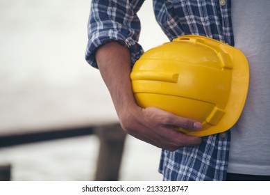 Engineer Man Hands Holding Hardhat White Work Helmet Hard Hat For Civil Construction Engineering. Construction Engineer Man In Safety Suit Hold White Work Helmet Hard Hat On Hands At Construction Site