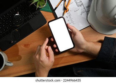 Engineer man hands holding smart phone over his workstation. Top view, blank screen for your advertise - Powered by Shutterstock