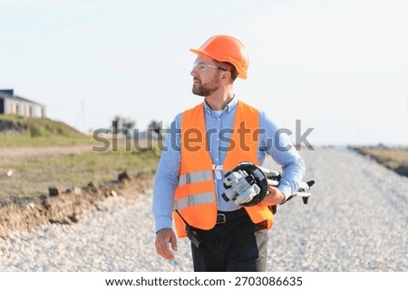 Engineer man inspecting roadwork progress, carrying professional surveying equipment, wearing safety vest and hard hat
