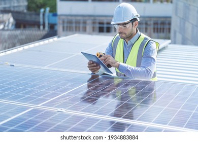 Engineer Man Inspects Construction Of Solar Cell Panel Or Photovoltaic Cell By Electronic Device. Industrial Renewable Energy Of Green Power. Factory Worker Working On Tower Roof.