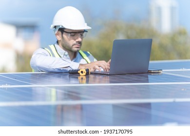 Engineer Man Inspects Construction Of Solar Cell Panel Or Photovoltaic Cell By Laptop Device. Industrial Renewable Energy Of Green Power. Factory Worker Working On Tower Roof And Skyscraper City.