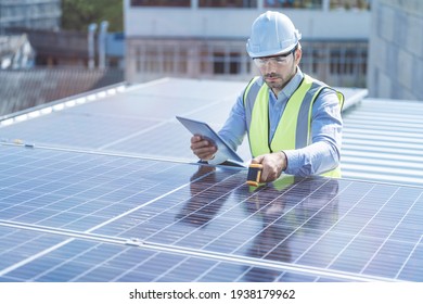Engineer Man Inspects Construction Of Solar Cell Panel Or Photovoltaic Cell By Electronic Device. Industrial Renewable Energy Of Green Power. Factory Worker Working On Tower Roof.