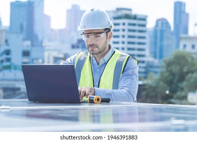 engineer man inspects construction of solar cell panel or photovoltaic cell by laptop device. Industrial Renewable energy of green power. factory worker working on tower roof and skyscraper city.