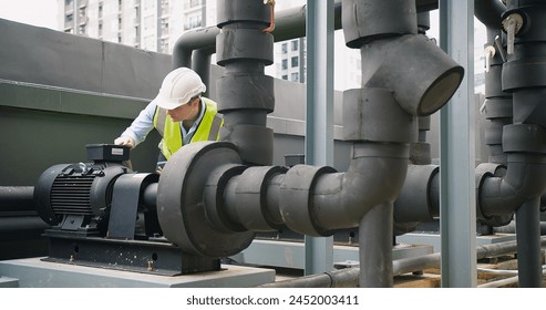 A Engineer man looking inspecting maintenance insulated pipelines valve pump control on the roof at an industrial site. He is wearing a hard hat and safety vest