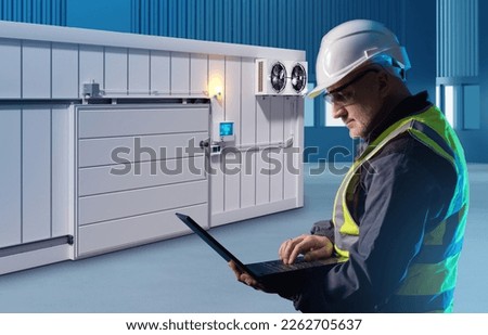 Engineer man near freezer. Worker controls warehouse refrigerator. Warehouse employee with laptop. Industrial refrigeration equipment. Container refrigerator for frozen food. Man control refrigerator