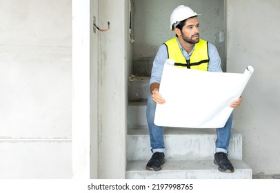 Engineer Man Reading Blueprint As Sitting At Home Improvement Construction Site. Professional Architect Wears Safety Hardhat Is Working On Home Interior, Housing Development Project. Copy Space.