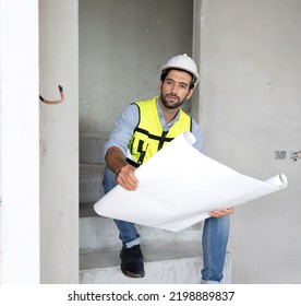 Engineer Man Reading Blueprint As Sitting At Home Improvement Construction Site. Professional Architect Wears Safety Hardhat Is Working On Home Interior, Housing Development Project. Copy Space.