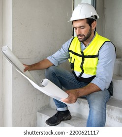 Engineer Man Reading Blueprint As Sitting At Home Improvement Construction Site. Professional Architect Wears Safety Hardhat Is Working On Home Interior, Housing Development Project. Copy Space.