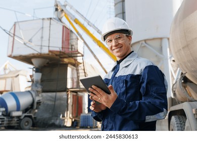 Engineer man in uniform with tablet computer controls loading of cement to mixer truck on concrete factory. Concept automated logistics on industry with online internet.
