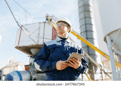 Engineer man in uniform with tablet computer controls loading of cement to mixer truck on factory. Concept banner automated logistics online internet.
