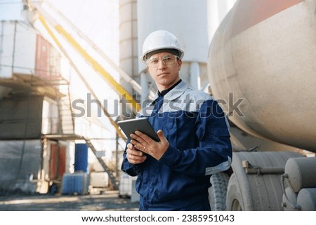 Engineer man in uniform with tablet computer controls loading of cement to mixer truck on factory. Concept banner automated logistics online internet.