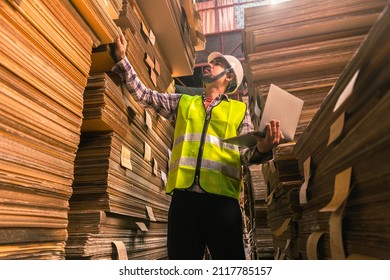 Engineer Man Wearing Safety Helmet And Vest Holding Clipboard And Take Note On The Paper In The Automotive Part Warehouse.Products And Corrugated Cardboard. Factory For The Manufacture Of Paper.