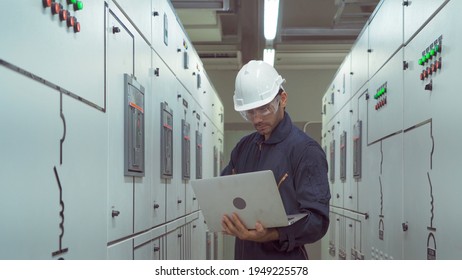 An Engineer Man Or Worker, People Using A Laptop Computer, Working In Electrical Room. Power Energy Motor Machinery Cabinets In Control Or Server Room, Operator Station Network In Industry Factory.