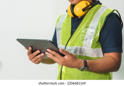 Engineer Man Working On Digital Tablet Computer At Worksite Or Industry. Handsome Young Industrial Worker Were Hard Hat, Safety Glove, Safety Glasses, Headphones. Blue Collar Worker. Isolated On White