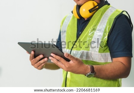 Engineer man working on digital tablet computer at worksite or industry. Handsome young industrial worker were hard hat, safety glove, safety glasses, headphones. Blue collar worker. isolated on white