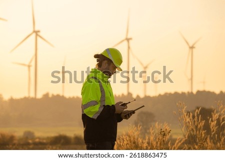 Engineer man working with tablet at windmill farm Generating electricity clean energy. Wind turbine farm generator by alternative green energy.