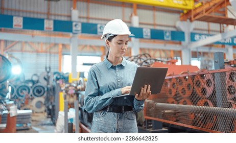 Engineer manager leader woman wearing helmet holding laptop standing and check in workplace area at manufacturing factory. Factory and Industrial plant concept - Powered by Shutterstock