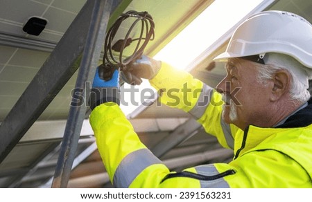 Engineer managing cables behind solar panels at a solar farm. Alternative energy ecological concept image.