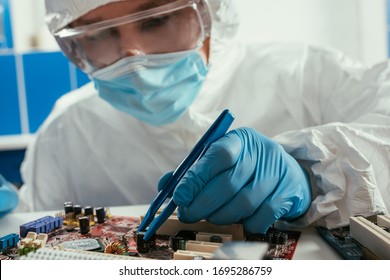 engineer in medical mask and goggles fixing computer motherboard with tweezers