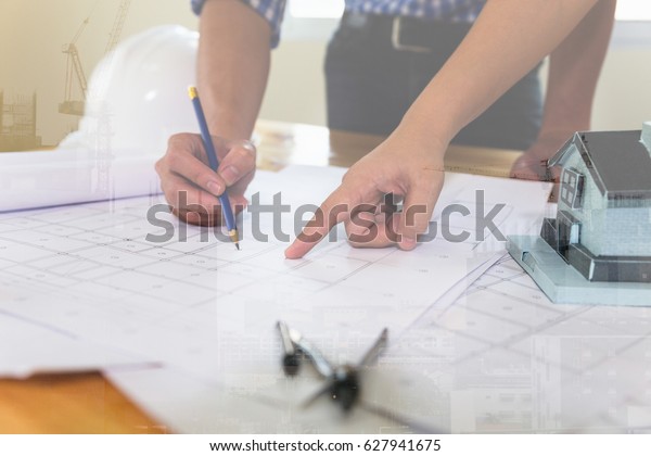 engineer meeting for architectural project,\
working with partner and engineering tools at workplace. Architect\
working on blueprint, double exposure with crane and building under\
construction