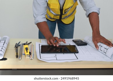 An engineer meticulously draws house plans on a workbench, surrounded by tools and blueprints, demonstrating precision and expertise in architectural design and construction planning. - Powered by Shutterstock