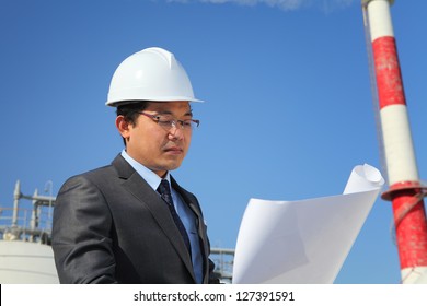  engineer oil refinery checking plan on location site with tower and blue sky background