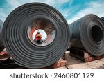 Engineer one worker man inspection on rolls of metal carbon steel sheets outside the factory or warehouse.