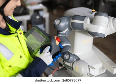 Engineer operating collaborative robot (cobot) using a handheld control panel in a smart factory. Industrial automation, robotics technology, and innovation in manufacturing process efficiency.