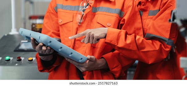 Engineer in orange jackets are looking at a tablet. One of them is pointing at something on the screen