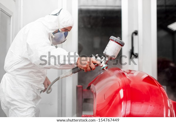 Engineer painting a red part of car with spray gun\
in special booth