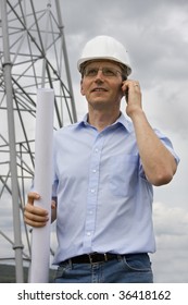 Engineer With Plan In His Hand Talking On Cell Phone On Construction Side