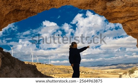 Engineer points at wind turbines from inside a cave, symbolizing the transition to clean energy sources