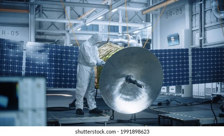 Engineer In Protective Suit Working On Satellite Construction. Aerospace Agency Manufacturing Facility: Scientists Developing Spacecraft For Space Exploration, Communications, Cosmos Observation