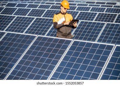 Engineer in protective workwear carrying out service of solar panels with digital tablet on a photovoltaic rooftop plant. Concept of maintenance and setup of solar power station - Shutterstock ID 1552053857
