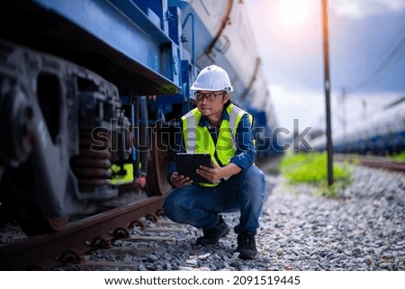 Engineer railway under checking construction process oil cargo train and checking railway work on railroad station with tablet  .Engineer wearing safety uniform and safety helmet in work.