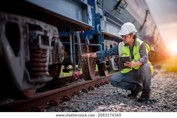 Engineer railway under checking construction\
process oil cargo train and checking railway work on railroad\
station with tablet  .Engineer wearing safety uniform and safety\
helmet in work.