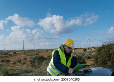 Engineer reviewing blueprints at a wind turbine farm, contributing to clean and sustainable energy production - Powered by Shutterstock