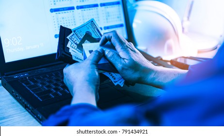 Engineer 's hand with us dollars banknotes and credit cards, on top of the notebook keyboard with helmet hard hat in background. Business and finance concept.