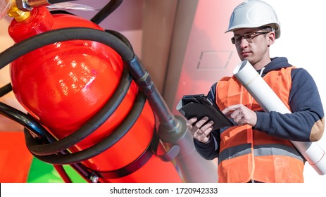 Engineer Of Safety Engineering. Checking Fire Extinguishers In The Building. A Man In A White Hard Hat With An Electronic Tablet In His Hands Against The Background Of A Fire Extinguisher.