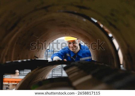 Engineer in safety gear checking interior of rotary die-cut mold, viewed through the cylinder in industrial environment. Unique visual emphasizing inspection and machinery.
