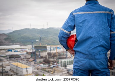 Engineer In Safety Suit Stand In Front Of Nuclear Construction