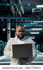 Engineer in server farm managing infrastructure systems, checking recovery plan on laptop. Data center worker monitoring performance using automation tools, making sure rigs are functioning optimally