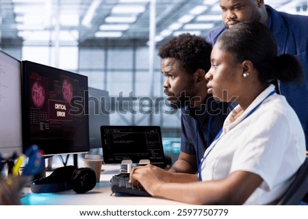 Engineer in server hub helped by coworkers to investigate breach alerts, working to protect equipment from hacker. Employee and colleagues using professional tools to mitigate security risks